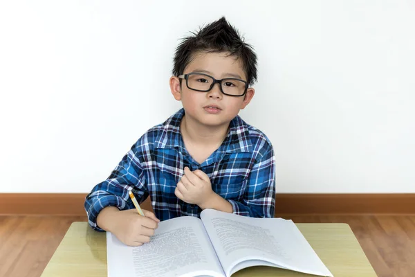 Little student boy in glasses doing his homework on the table