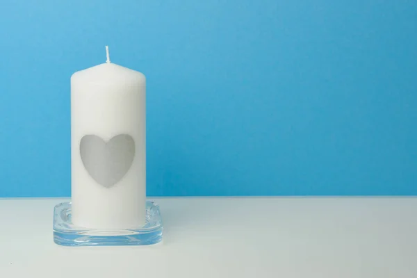 white candle with a heart on it in front of colorful background