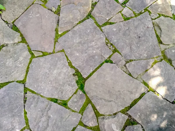 Каменный пол, Каменная стена из большого гранитного булыжника крупным планом. Растущий зеленый мох между швами — стоковое фото