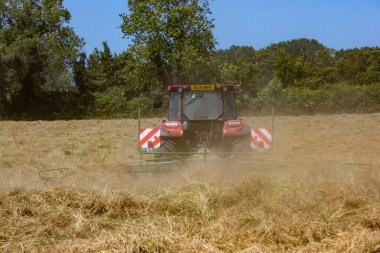 Hay Hasat Haziran 2020 İngiliz kırmızı traktörü, onu baltalamak için saman dönüyor, mavi gökyüzü güneşli bir gün. Güneş parlarken saman yap. Hampshire İngiltere