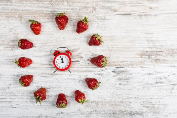 strawberry clock without hands with an alarm clock in the middle on a wooden vintage board