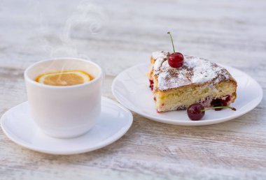 Kirazlı turta beyaz bir tabak ve beyaz fincan limon ile çay lezzetli bir parça. Yakın çekim. MoCap.