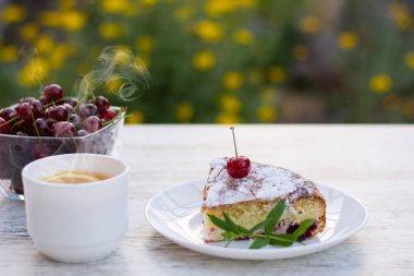 Kirazlı turta beyaz bir tabak ve beyaz fincan çay limon ve nane ile lezzetli bir parça. Yakın çekim. MoCap.