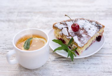 Beyaz bir tabak ve limon ve nane ile sıcak çay beyaz bir fincan kiraz pasta lezzetli bir parça. Close. Mocap, ne kadar çok şey var? Alanı, metin için alanı kopyalama.