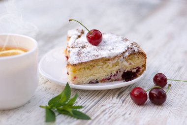 Beyaz bir tabak ve limon ve nane ile sıcak çay beyaz bir fincan kiraz pasta lezzetli bir parça. Close. Mocap, ne kadar çok şey var? Alanı, metin için alanı kopyalama.