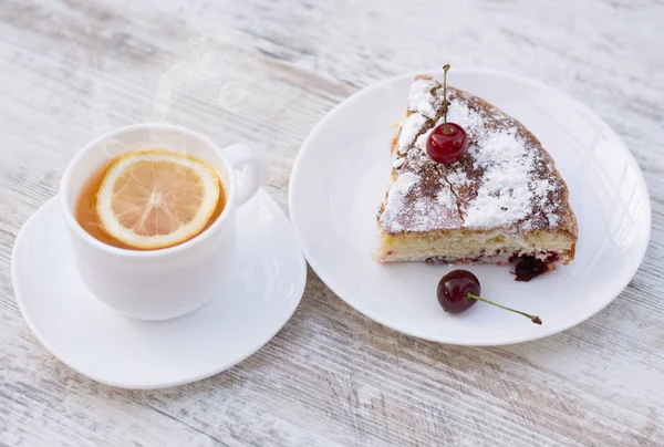 Kirazlı turta beyaz bir tabak ve beyaz fincan limon ile çay lezzetli bir parça. Yakın çekim. MoCap.