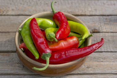 Ahşap arka plan üzerinde kahverengi bir seramik tabak içinde yatan kırmızı ve yeşil acı, acı biber