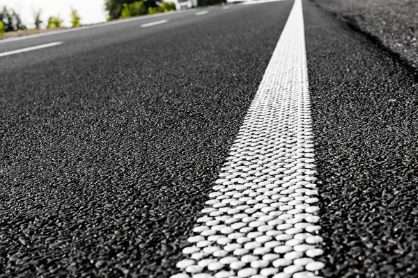 New black asphalt road and dividing lines from white dots. Textural background of asphalt.