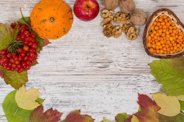 Autumn background. Berries and leaves of viburnum, sea buckthorn, pumpkin, walnuts, red apple, on a light wooden background, top view. Copy space, flatly