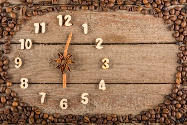 Decorative clock with wooden numerals and arrows made of cinnamon sticks, showing 6 o'clock, on a wooden background and a frame of coffee beans. Kitchen, advertising, banner, Copy space, flatly.