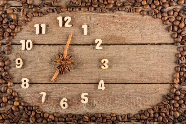 Decorative clock with wooden numerals and arrows made of cinnamon sticks, showing 7 o\'clock, on a wooden background and a frame of coffee beans. Kitchen, advertising, banner, Copy space, flatly.