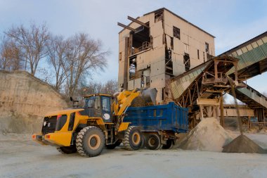 Sarı Ekskavatör kova içine büyük bir yığın moloz toplar ve kamyonun içine dökülen. Taş ocağı, madencilik ve taş sürtünme.