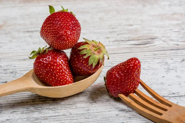 Summer vitamin food. Lots of fresh ripe fragrant strawberries and a wooden spoon and fork, lie on a textured light wooden background. Food causing allergies. Copy space