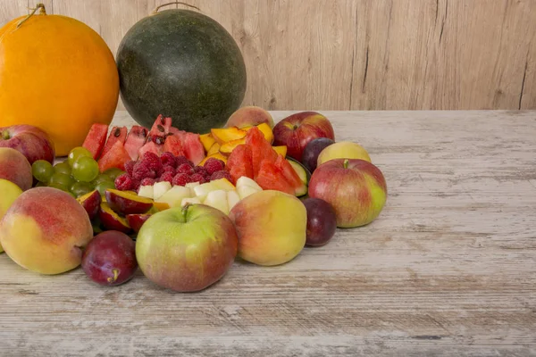 Fruit mix. Apple, peach, grapes, watermelon, cantaloupe, raspberry, plum. Whole fruits and slices on a plate lie on a white wooden background. Copy space, Place for text.