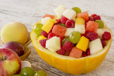 Meyve salatası. Şeftali, karpuz, kavun, ahududu, Erik, üzüm, kavun salata kasesi Beyaz ahşap zemin üzerine doğranmış yalan. Tüm meyve tahta kaşıklar içinde. Metin için yer. Kopya alanı. 