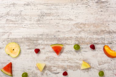 Adet meyve, elma, şeftali, kavun, karpuz, üzüm, Erik, ahududu, dokulu bir ışık ahşap arka plan üzerinde yalan. Düz üst görünümü, metin için yer. Yat, alanı Kopyala. Yaz arka plan.