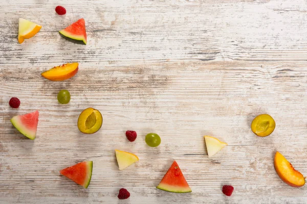 Pieces of fruit, apple, peach, melon, watermelon, grapes, plum, raspberry, lie on a textured light wooden background. Flat top view, place for text. Flat Lay, Copy Space. Summer background.