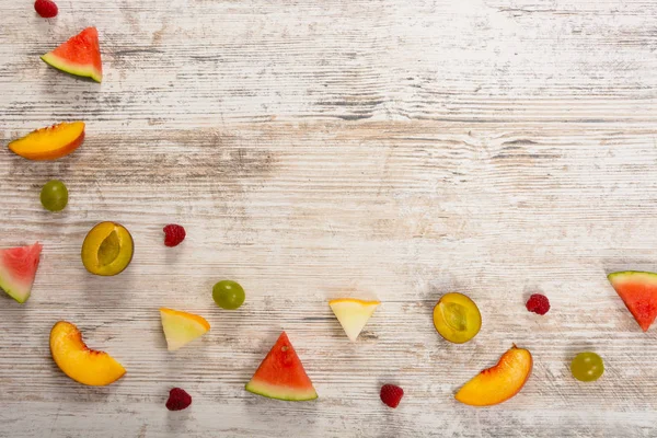 Adet meyve, elma, şeftali, kavun, karpuz, üzüm, Erik, ahududu, dokulu bir ışık ahşap arka plan üzerinde yalan. Düz üst görünümü, metin için yer. Yat, alanı Kopyala. Yaz arka plan.