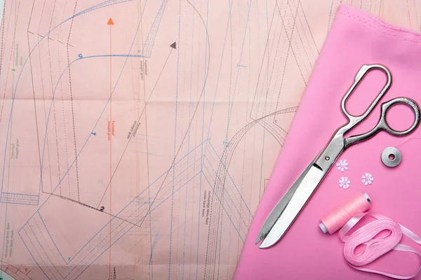 Tailoring. Sewing accessories and accessories for sewing and needlework. Scissors, centimeter, pattern, reel with thread and fabric of pink color. Flat Lay, Copy Space