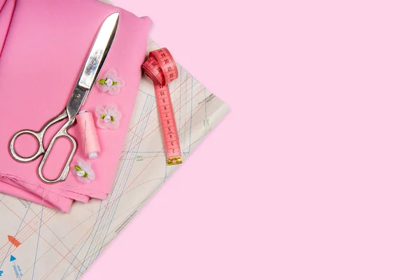 Tailoring. Sewing accessories and accessories for sewing and needlework. Scissors, centimeter, pattern, spool of thread and fabric of pink color on a pink background. Isolate, Flat Lay, Copy Space