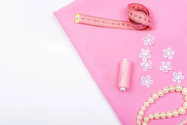 Tailoring. Sewing accessories and accessories for sewing and needlework. Imitation jewelry, centimeter, pattern, reel with thread and fabric of pink color on a white background. Isolate, Flat Lay, Copy Space