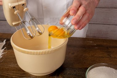 Elinde elektrikli mikser olan bir şef, yumurtaları tahta bir masanın üzerindeki bir kapta yener. Yemek pişirmek için malzemeler. Yan görünüm, Kopya alanı, metin için alan.