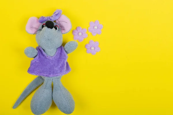 Plush toy mouse in a dress and a lilac bow on a yellow background. Flat Lay, Copy space, space for text.