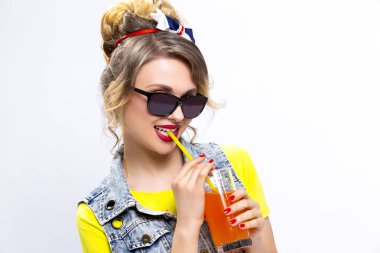 Mutlu bir hayat fikirler ve kavramlar. İyimser ve mutlu beyaz sarışın kızla portakal suyu ve saman. Denim yelek ve güneş gözlüğü takıyor. Beyaz karşı. Yatay yönlendirme