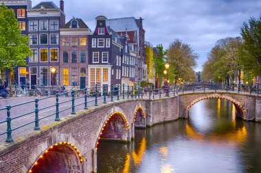 Amsterdam Cityscape kendi kanalları ile Nighview. Işıklı köprü ve geleneksel Hollanda evleri arka planda alacakaranlıkta. Yatay atış
