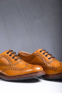 Lüks erkek tam Broggued Tan deri Oxfords ayakkabı beyaz yüzey üzerinde aşırı Closeup. Gri duvara. Dikey görüntü kompozisyon