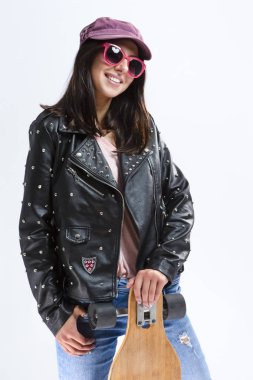 Modern gençlik kavramları. Mutlu gülümseyen beyaz esmer siyah deri ceket ve Longboard ile poz güneş gözlüğü portresi. White.Vertical yönlendirme üzerinde