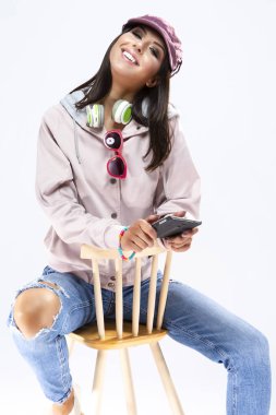 Akıllı telefon ve kulaklık giyen ile poz mutlu gülümseyen esmer beyaz kız portresi. Beyaz karşı. Dikey atış