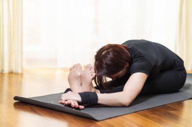 Yoga kavramı. Kafkas kadın Yoga egzersiz kapalı parlak öğleden sonra itibariyle uygulamak. Pashchimottasana poz yalnızlık meditasyon oturumu sırasında oturan. En iyi siyah sütyen ve siyah Pants.Horizontal görüntü