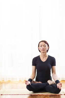 Kafkas kadın pratiği Yoga kapalı. Sukhasana Lotus poz Indoors.In büyük güneşli penceresinin önünde oturuyor. Dikey kompozisyon