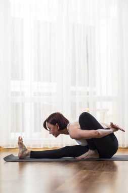 Pratik yoga Asana kapalı büyük güneşli pencerenin önünde kadın. Oturan iken bir bacak gerili ileri ve ellerini çapraz Behind.Vertical görüntü