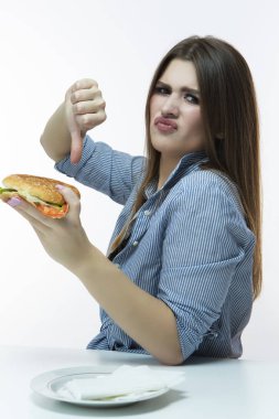 Sağlıksız yeme kavramları. Burger baş parmakları bakarak kafkas kadın. Studio.Vertical görüntü kompozisyon içinde kapalı plaka ile poz
