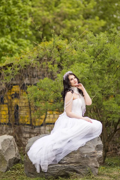 Sensual Caucasian Bride With Diadem Sitting On Stone In Flowers
