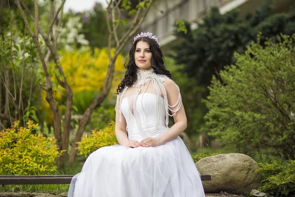 Portrait of Caucasian Bride With Diadem Sitting In Flowers Garden