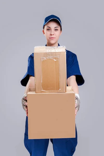 Delivery Services Ideas. Portrait of Positive Caucasian Female Messenger With Variety Disptatched Freight of Carton Boxes. Against Gray. Vertical Image