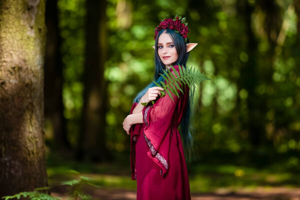 Costume Play Ideas. Forest Sprite in Flowery Garland Posing with Elf Enlarged Ears in Summer Forest With Fern Leaves. Horizontal Image Composition