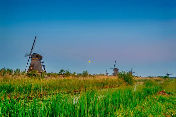 Dutch Destinations Concepts. Line of Traditional Romantic Dutch Windmills in Kinderdijk Village in the Netherlands During Blue Hour. Horizontal Image