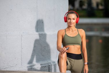 Açık havada esneme egzersizleri sırasında Koşu Kıyafetinde Profesyonel Kafkas Kadın Atleti. Kulaklıkla müzik dinlemek. Yatay Çekim