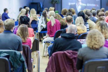 Konferans sırasında büyük bir grup dinleyici önde ekrana bakıyor. Yatay çekim