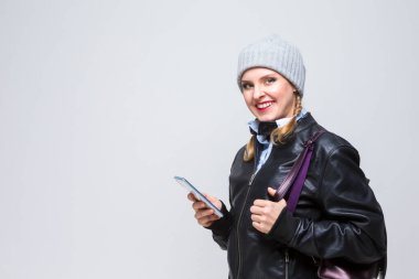 Sırtında cep telefonu ve sırt çantalı, kalın şapkalı, deri ceketli mutlu beyaz kız. Yatay Resim