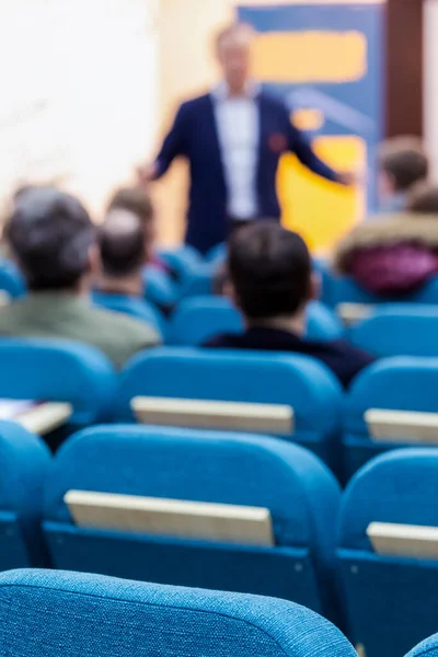 People At Conference Listening to Presenter In Front of a Group of Listeneres Standing in Front of The Big Screen. Vertical Image Orientation