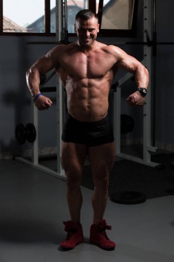 Yakışıklı Genç Adam Spor Salonunda Güçlü Duruyor ve Kaslarını Geriyor - Kas Atletik Vücut Geliştirici Spor Sonrası Spor Pozisyonu