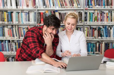 Kütüphanede dizüstü bilgisayar ve A yüksek çalışma kitapları yakışıklı iki üniversite öğrencileri üniversite kütüphanesi okul.