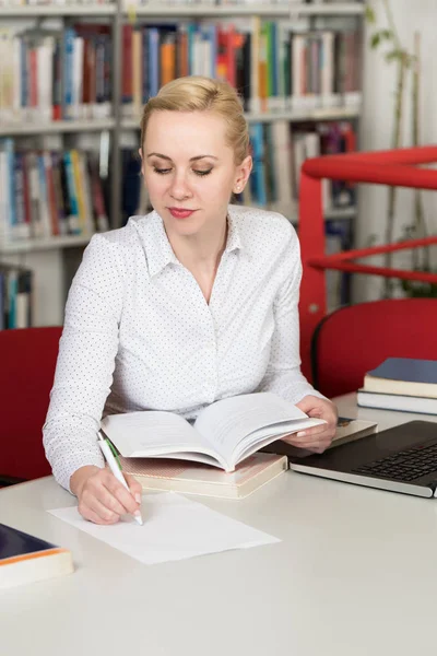 Bir yüksek okul kütüphanesinde çalışma kitapları ile güzel kız öğrenci