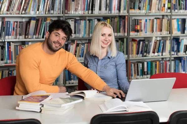 在图书馆英俊的两个大学生与笔记本电脑和书籍工作在一个高中大学图书馆 — 图库照片