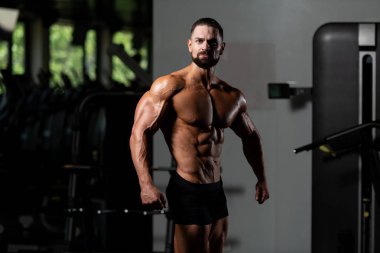 Yakışıklı Genç Adam Spor Salonunda Güçlü Duruyor ve Kaslarını Geriyor - Kas Atletik Vücut Geliştirici Spor Sonrası Spor Pozisyonu